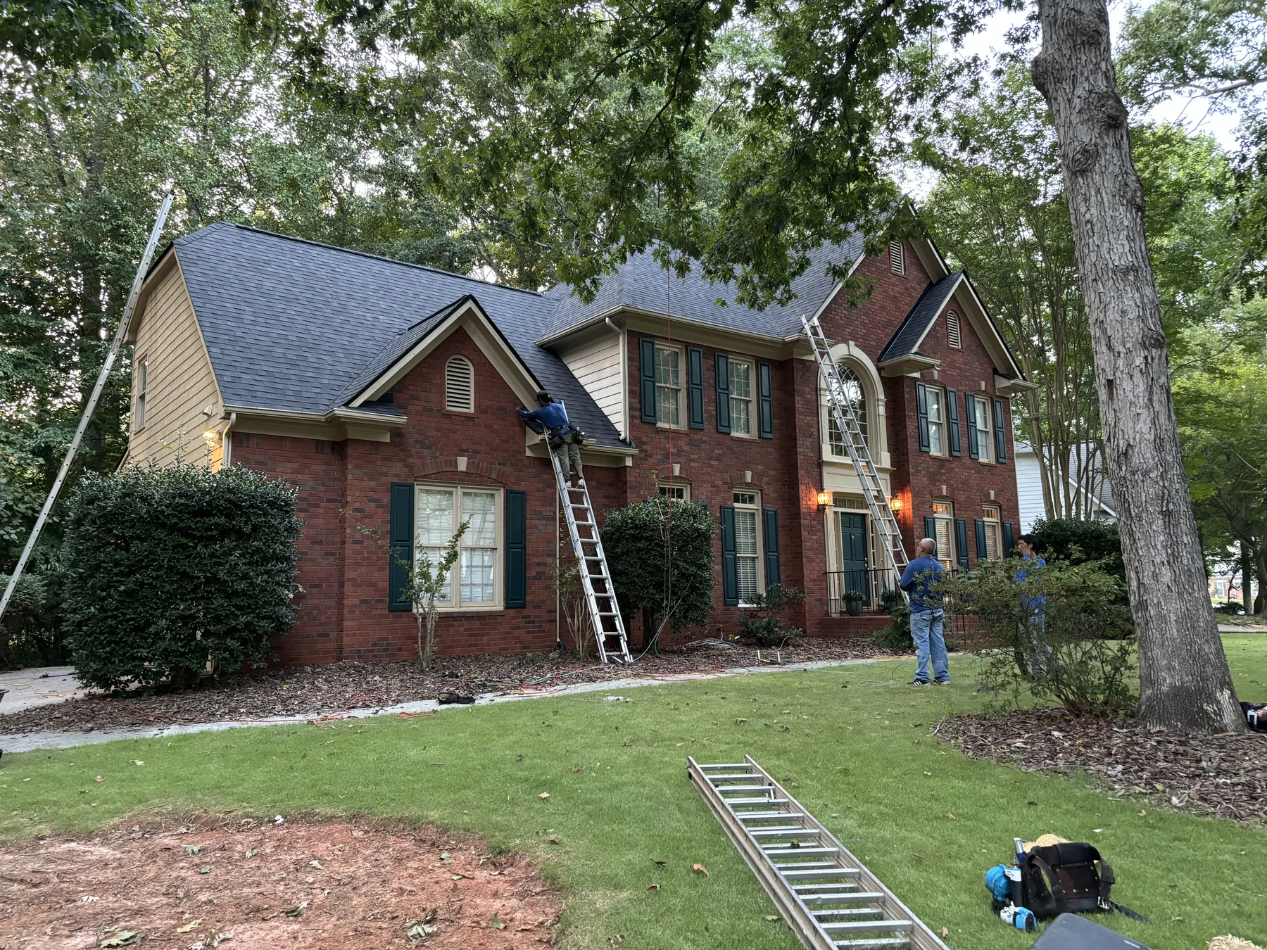 Roof replacement work on a brick home with crew and ladders